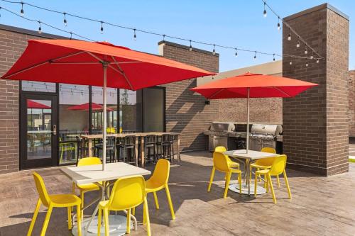 a patio with tables and yellow chairs and red umbrellas at Home2 Suites By Hilton Milwaukee West in West Allis