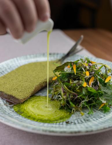 a person pouring sauce on a plate with a salad at Arche Hotel Wrocław Airport in Wrocław
