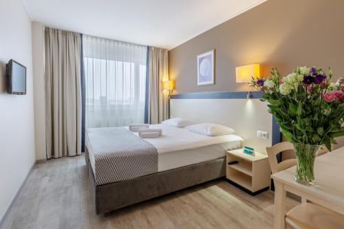a hotel room with a bed and a vase of flowers at Aurora Hotel Klaipeda in Klaipėda