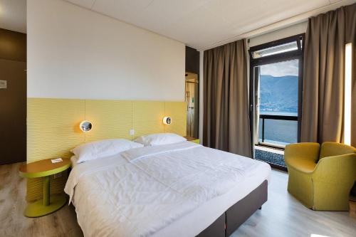 a bedroom with a bed and a chair and a window at Parkhotel Brenscino Brissago in Brissago