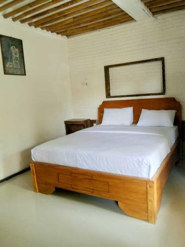 um quarto com uma cama de madeira e lençóis brancos em Gubuk Baru Homestay em Tetebatu