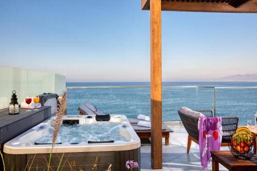 een hot tub op een terras met de oceaan op de achtergrond bij Hersonissos Beach Front Suites in Chersonissos
