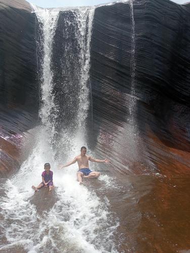 two men sitting in the water next to a waterfall at รี่สอตน้ำตกถ้ำพระ in Ban Non Sung
