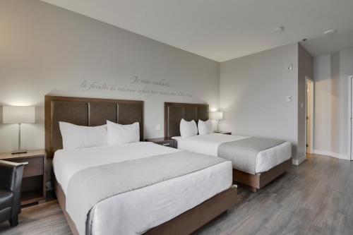 a hotel room with two beds and a chair at Hôtel et Pavillons Le Petit Manoir du Casino in La Malbaie