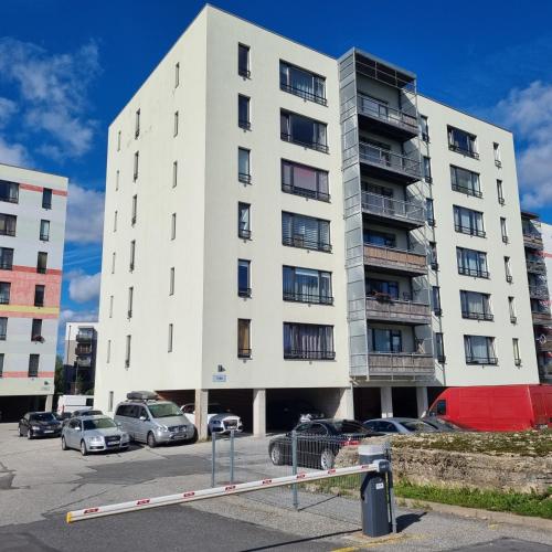 a tall white building with cars parked in a parking lot at Beautiful apartment with sauna in Tallinn