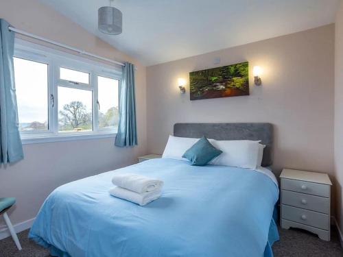 a bedroom with a bed with blue sheets and two windows at Kilninver Chalet on Reelig Estate Near Inverness in Kirkhill