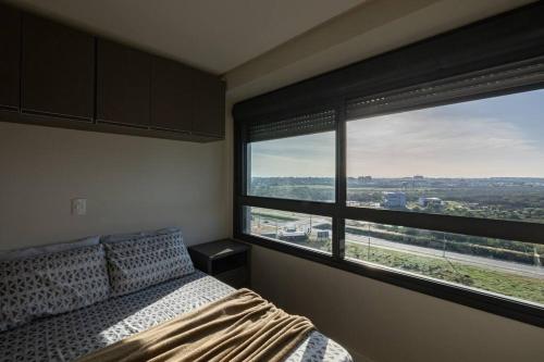 a bedroom with a bed and a large window at Studio encantador no Parque Una com estacionamento incluído in Pelotas