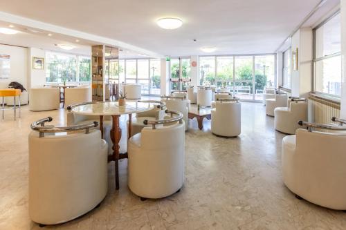 a restaurant with white chairs and tables and windows at Hotel Naica in Rimini