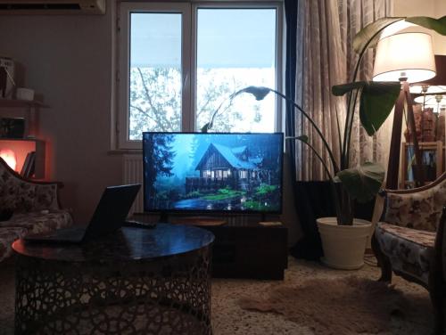 una sala de estar con TV y una casa en la pantalla en Garden Village Home, en Ayvalık