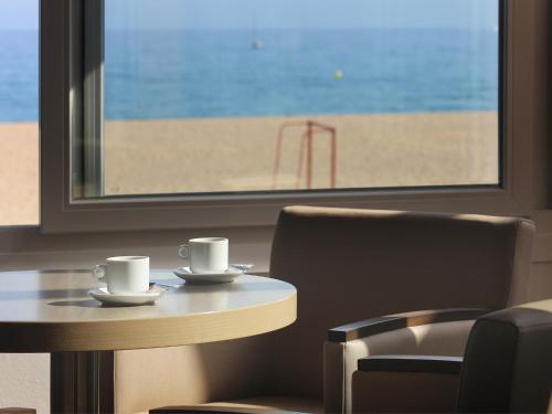 two coffee cups sitting on a table in front of a beach at Rocatel in Canet de Mar