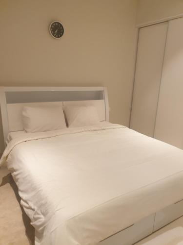 a bed with white sheets and a clock on the wall at Beautiful Golf & Sea View in As Sīfah