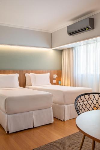 two beds in a hotel room with a table and chairs at INNSiDE by Meliá São Paulo Iguatemi in Sao Paulo