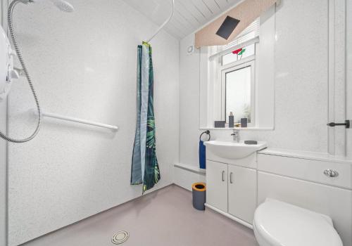 La salle de bains blanche est pourvue d'une douche et d'un lavabo. dans l'établissement Back'o'Barns Apartment by Klass Living Hamilton, à Hamilton