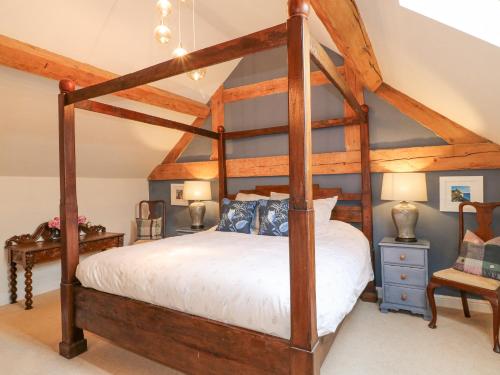 a bedroom with a wooden canopy bed with white sheets at Dovecote Cottage in Ashbourne