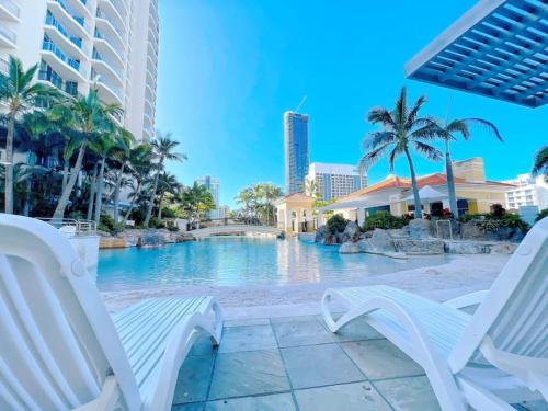 a resort pool with white chairs and palm trees at Prime Location 2BD Serviced Apt at Surfers Paradise in Gold Coast