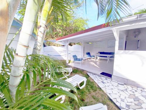 a white house with white furniture and a palm tree at La Rose du Bresil Marie-Galante in Capesterre-de-Marie-Galante