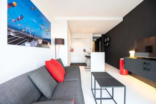 ein Wohnzimmer mit einem grauen Sofa und einem roten Kissen in der Unterkunft Luxe appartement Eliza - frontaal zeezicht in Mariakerke in Ostende