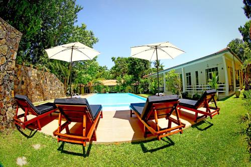 a pool with chairs and umbrellas in front of a house at Beach Grove Villas in Unawatuna