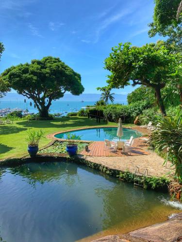a pool in a yard with trees and a beach at Casas D’Água Doce - Casa da Árvore in Ilhabela
