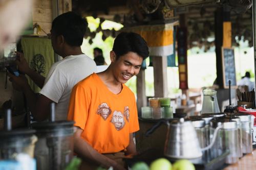 a man in an orange shirt standing in a kitchen at Sweet Orange Pondok in Ubud