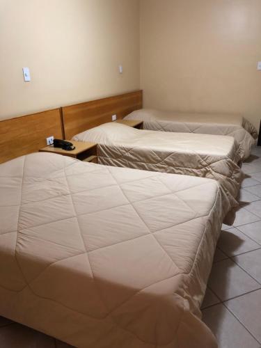 two beds in a hotel room with white sheets at Hotel Villa de Minas in Monte Sião