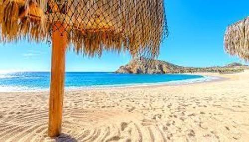 una sombrilla de paja en una playa con el océano en Excelsior Residence, en Cabo San Lucas