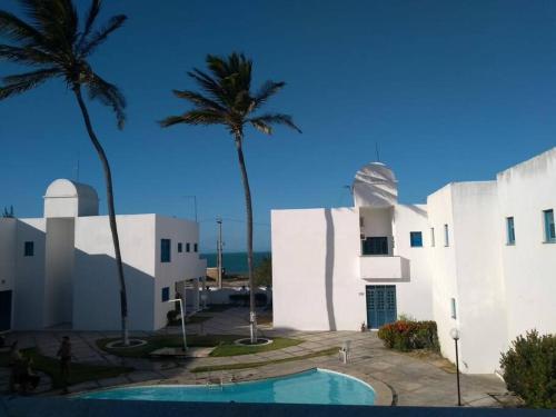 a white building with palm trees and a swimming pool at Paraiso frente ao mar, réplica de uma vila grega! in Aracati