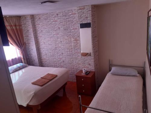 Habitación pequeña con 2 camas y pared de ladrillo en Hostal El Auténtico Diamante, en Quito