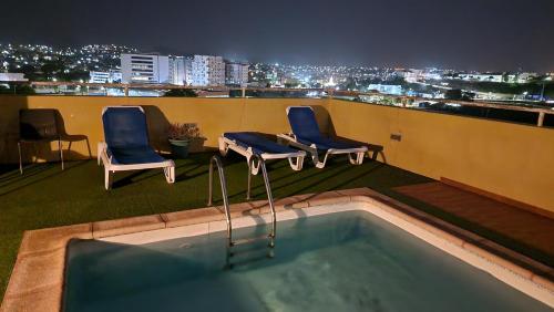 two chairs and a pool on a rooftop at night at Casa de férias com 2 quartos ou aluguer diária in Praia