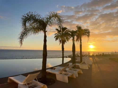 a pool with palm trees and chairs and a sunset at Suite CU - Sea View - 3 Pools - AC - Free Park - Free Gym in Funchal
