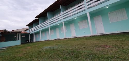 a blue building with white doors and a grass field at Vila Mar Flats - 1 Dorm - Guriri - 800m da Praia in Guriri