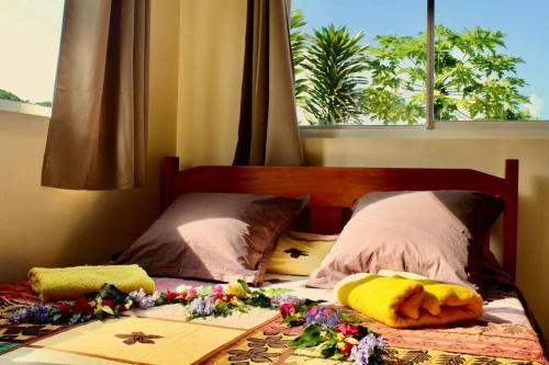 ein Bett mit Blumen und einem Fenster in der Unterkunft Tekauhivai Lodge in Uturoa