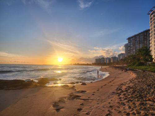 a beach at sunset with the ocean and buildings at Breathtaking 2-Bedroom Beachside Apartment in San Juan