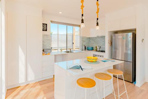 a white kitchen with a counter and two stools at Private and peaceful house near the Beach in Coolum Beach