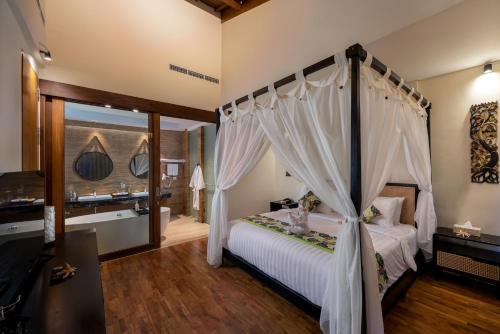 a bedroom with a canopy bed and a bathroom at Mokko Suites Batubelig in Canggu