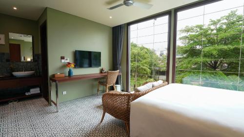 a bedroom with a bed and a desk and a window at CHiEM HoiAn - The Beachside Boutique Hotel & Villa in Hoi An