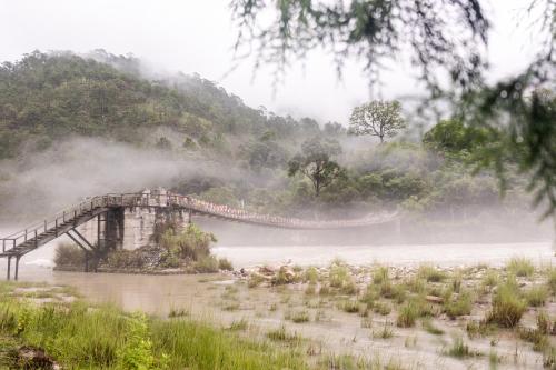 a bridge in the middle of a river with fog at Pemako Punakha in Punākha