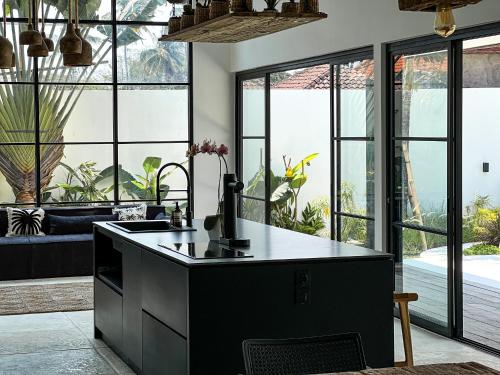 KAKAO Villas Kedungu في تاناه لوت: مطبخ مع جزيرة سوداء في غرفة مع نوافذ