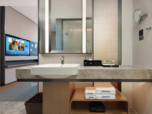 a bathroom with a sink and a mirror and a tv at Hampton by Hilton Shenzhen Bao'an Airport in Shenzhen