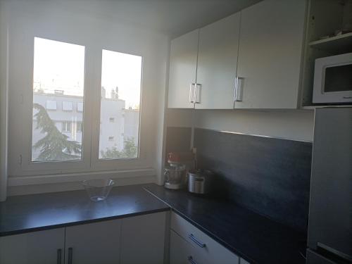 a kitchen with white cabinets and a black counter top at Appartement cosy 6 personnes proche gare in Rueil-Malmaison