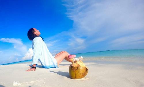 un homme assis sur une plage avec un panier dans l'établissement Wind Breeze Sunset View Inn, à Guraidhoo