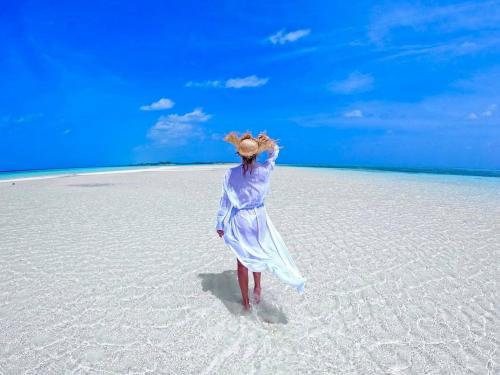 a woman in a blue dress standing on a beach at Wind Breeze Sunset View Inn in Guraidhoo