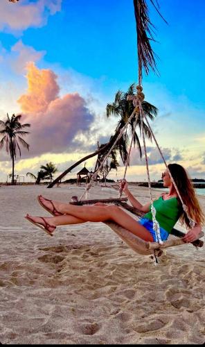a woman sitting on a swing on the beach at Wind Breeze Sunset View Inn in Guraidhoo