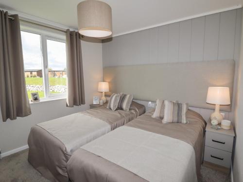 two beds in a room with two lamps and a window at 35 Delamere Point in Northwich