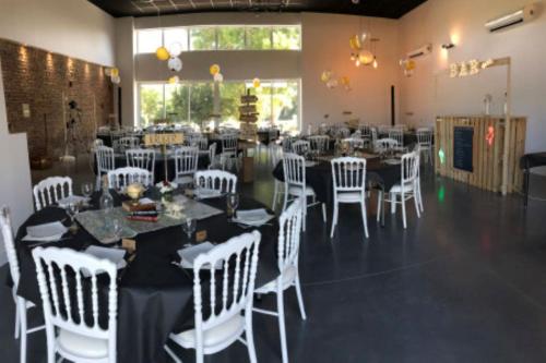 une salle de banquet avec des chaises et des tables blanches et une pièce avec des tables et des chaises blanches dans l'établissement Les Maisons de Ronsac : lieu idéal pour vos fêtes, à Saint-Pierre-de-Lages