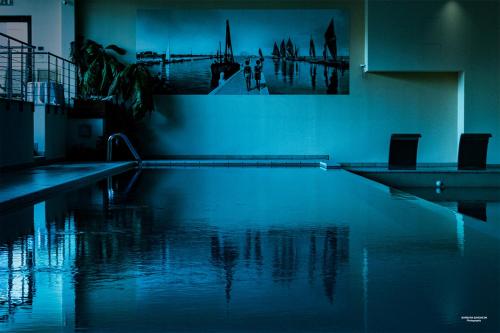 a swimming pool with two chairs and a painting on the wall at Hotel Dante Family Spa Resort in Cervia