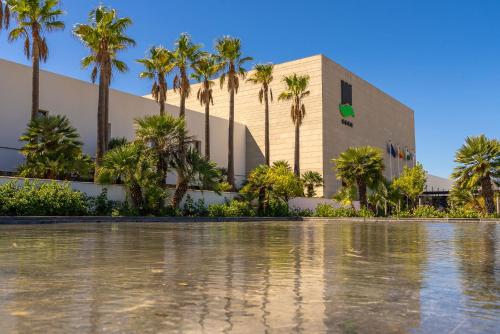 a building with palm trees in front of a body of water at Hotel Fuerte Conil-Resort in Conil de la Frontera