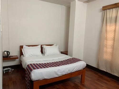 a bedroom with a bed with white sheets and a window at April Springs Home Stay in Shillong