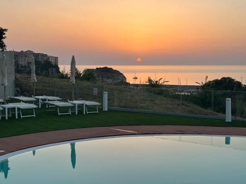 a sunset over a pool with tables and chairs at Residence New Paradise in Tropea