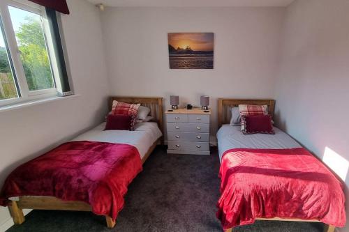 two twin beds in a room with two windows at Cornish Village Getaway in Gwennap